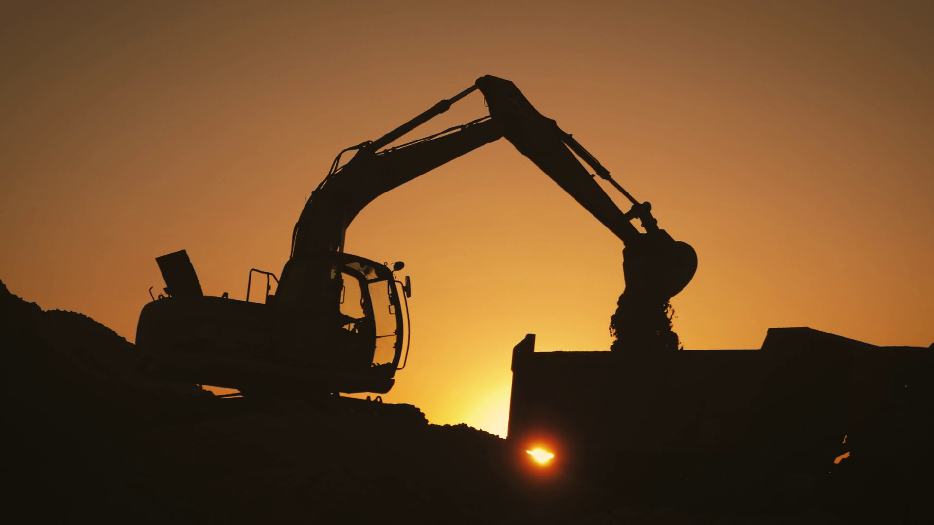Excavator kuning bekerja di lokasi konstruksi saat senja